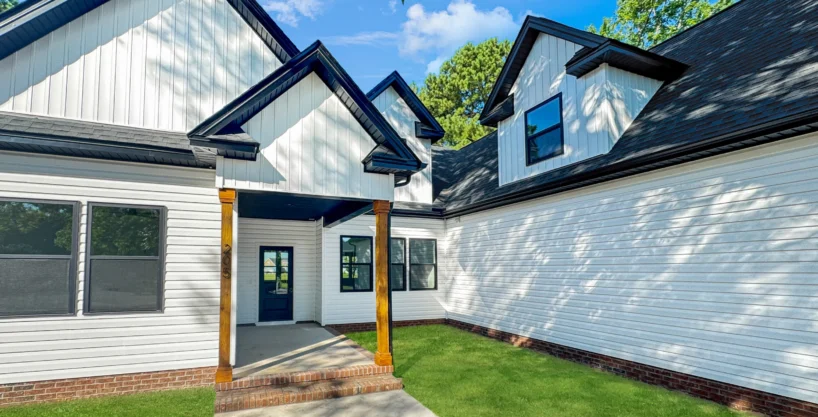 Exterior view of The Belhaven model home in Elizabeth City, NC, featuring white siding, black trim, and wood porch columns.